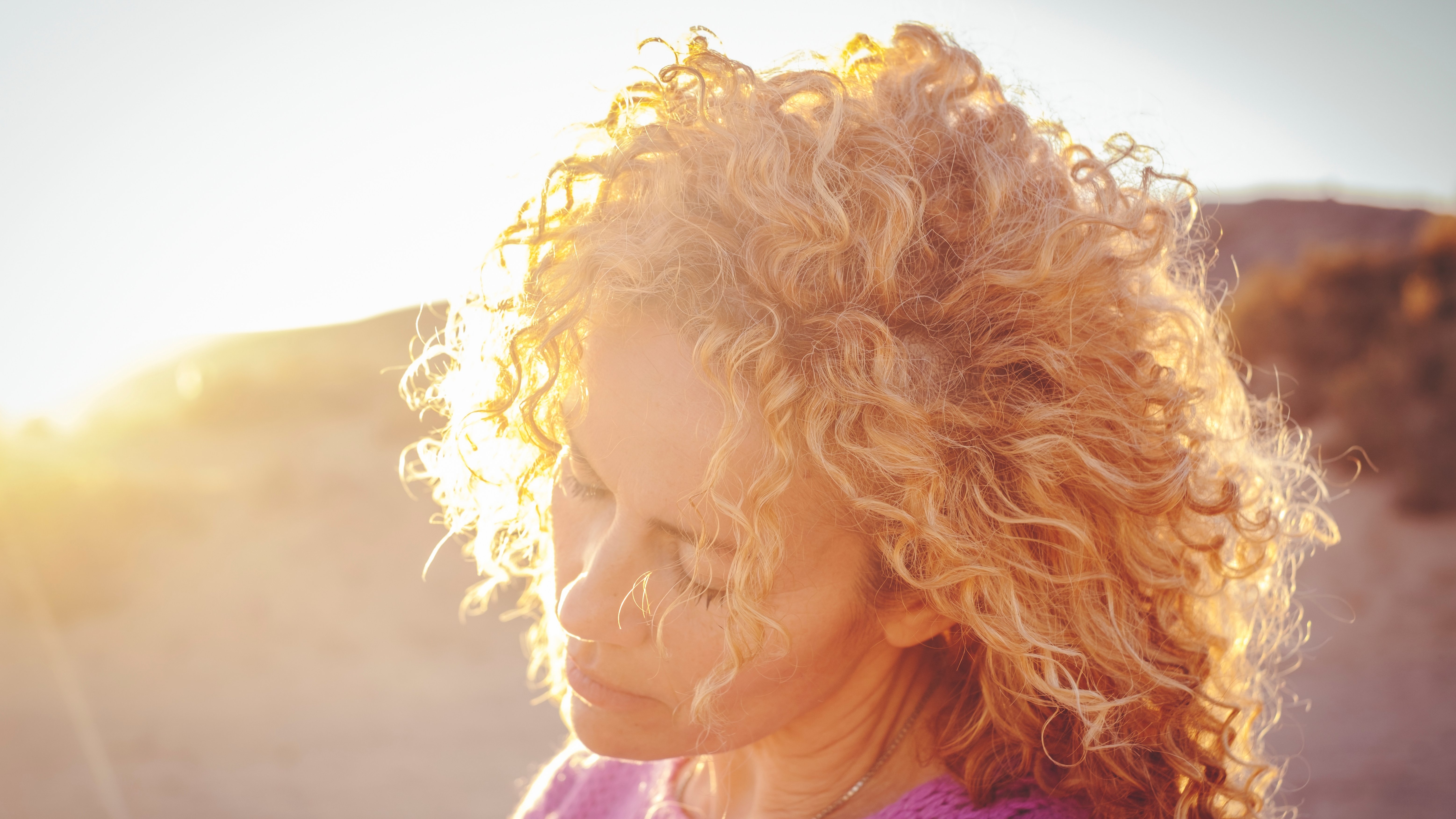 A woman with blonde curls being illuminated by the autumn sun.